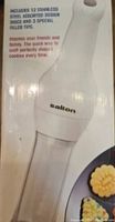 Photo of the Salton cookie press showing the handle and clear plastic barrel. Includes text about the 12 stainless steel design discs and 3 roller tips for making cookies.