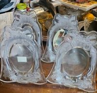 Photo showing four clear glass picture frames with decorative floral and bow motifs, about 8 inches tall.