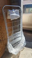 Image shows a silver metal grocery cart standing upright outside, with a clear plastic wrap at the base and an information paper attached to the front.