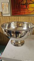 Photo of the large silver tone punch bowl from the exterior showing its polished reflective finish and pedestal base.