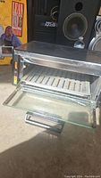 Photo showing a metal toaster oven with open glass door, wire rack inside, and control knobs on the side.