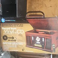 Photo of the box of the Innovative Technology wooden music center showing the recordable CD player, 3-speed turntable, cassette player, and AM/FM radio with remote included.