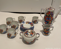 Full tea set arranged on table showing cups, saucers, teapot, creamer, sugar bowl, and container with colorful floral hand-painted designs.