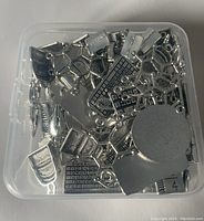 Top view of single plastic box filled with assorted silver-tone charms including shoe, heart, starfish, and keyboard shapes.