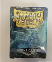 Front view of sealed package containing 100 Dragon Shield clear matte standard size card sleeves.