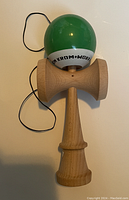 Front view of wooden kendama with green ball and string, showing KROM branding on tama.
