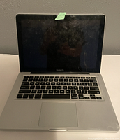 Opened Apple MacBook Pro laptop showing keyboard and screen with a piece of green tape on top edge of screen
