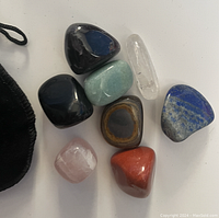 Top-down image of polished tumbled stones including black, light green, clear, blue, pink, reddish, and banded brown stones.