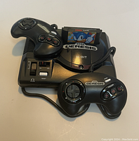 Ornament resembling Sega Genesis console with two controllers and Sonic cartridge shown on a flat surface.