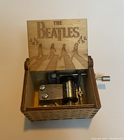 Open view of music box showing The Beatles Abbey Road engraving on lid and internal music mechanism with metal crank.
