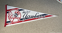 Photo of a vintage triangular New York Yankees pennant on carpeted floor, showing full design including team name, logo, and colors.