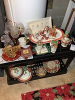 Photo showing an overview of various Christmas-themed dishes, glasses, and decorations on a black metal shelf in basement setting.