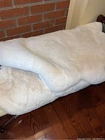 Two folded faux fur rugs on a wooden bench against a brick wall, showing thickness and plush texture.