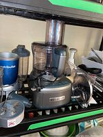 Grey Cuisinart food processor base with power cord, clear bowl, NutriBullet cup at left and Cuisinart blade attachment at front