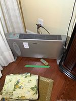 Clairion fan heater placed on floor near wall outlet with remote and some folded fabric nearby.