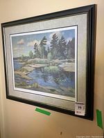 Full view of the framed print hanging on wall showing the landscape artwork with trees and water.