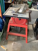 Front and side angled view of an orange Skil table saw with metal stand, showing rip fence and blade.