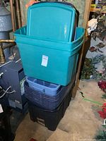 Stacked plastic storage totes with lids in teal, dark blue, and black colors in basement environment