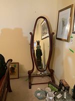Front view of full-length oval wooden framed mirror on stand in room.