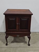 Front view of the antique style wooden cabinet with closed paneled double doors and cabriole legs.