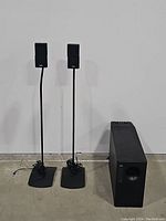 Two Bose speakers mounted on black adjustable stands alongside a Bose subwoofer on the floor.