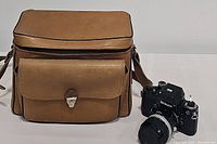 Tan brown leather camera bag with adjustable strap and Nikon camera body to right