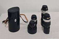 Four Nikon lenses and cylindrical carrying case grouped on white surface