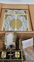 Box containing mechanical clock movement with visible brass gears and rods, some parts wrapped for protection.