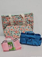 Set of four collapsible bags: a large floral print bag, a smaller floral shower bag, a blue multi-pocket shower tote, and a folded pink tote bag with striped handles