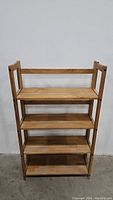 Front view of foldable bookshelf with four wooden shelves and side frame.