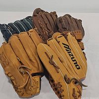 Five assorted baseball/softball gloves arranged in a row, showing overall condition and colors.