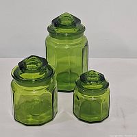 Three lidded green glass canisters of varying sizes displayed together on white surface