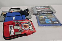 A photo showing Garage Boss branded tool organizer bag in red and black with multiple pockets and a blue and black tool bag with shoulder strap.