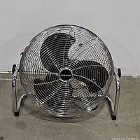 Front view of Black & Decker metal floor fan showing three black blades and chrome grille and frame on concrete floor.