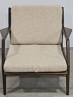 Front view of mid-century modern lounge chair with beige cushions and wooden frame.