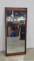 Front view of full rectangular mirror with solid wood frame, showing warehouse background.