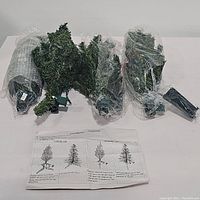 Four segmented pre-lit artificial fir trees and stands wrapped in clear plastic, placed on white surface with instruction sheet visible.