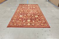 Full view of the rectangular red floral rug laid flat on floor displaying border and central floral pattern.