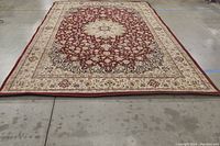 Full view of rectangular red patterned rug displaying central cream medallion and beige border with floral motifs.