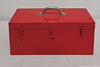 Closed red metal toolbox with silver handle and three latches (one center, two sides).