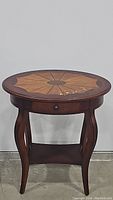 Front view of round two-toned wooden side table with sunburst pattern on top and curved legs.
