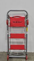 Front view of the Total Trolley in folded vertical position, showing red steps and handle with brand logo visible.