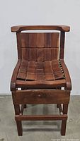 Front view of vintage wooden chair/stool showing woven seat and backrest with solid wood frame and curved armrests.
