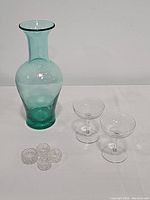 Green Blenko glass vase, pair of etched vintage champagne glasses and four crystal candlestick holders displayed on a white surface.