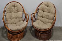 Photo showing the pair of vintage rattan swivel rocker lounge chairs side by side, highlighting the rounded rattan frame and beige tufted cushions.