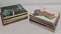 Two stacks of assorted vinyl record albums with visible varied cover art, one with a paddling scene person and the other with colorful abstract figures.