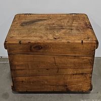 Front view of the closed wooden chest showing the natural wood surface with knots, scratches, and some wear.
