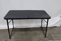 Full view of the black rectangular table unfolded, showing the vinyl surface and metal folding legs.