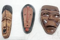 Three African wooden masks shown together on white background.