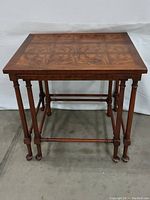 Front view of stacked nesting tables showing the smallest table on top with a patterned veneer surface and solid turned legs